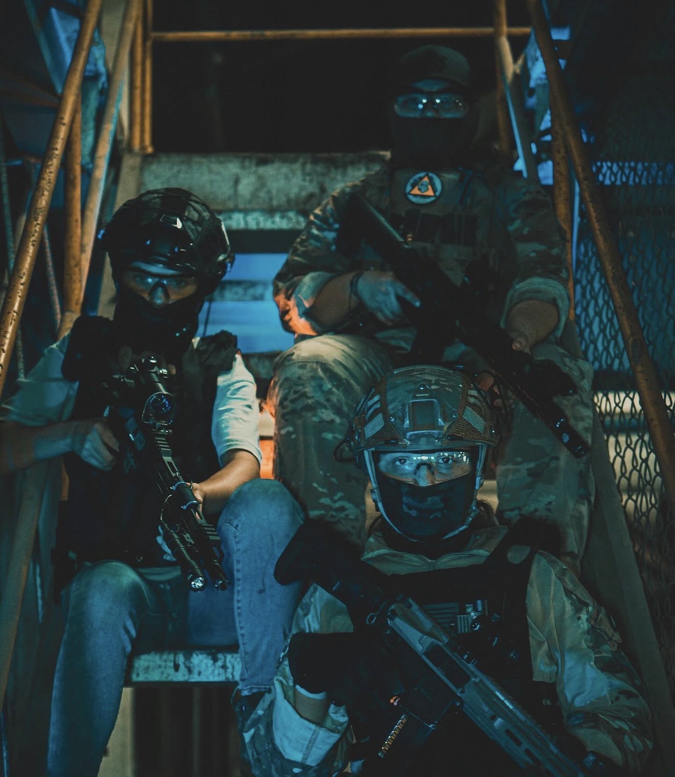 Tres jugadores de airsoft con sus réplicas y equipo de protección en una escalera